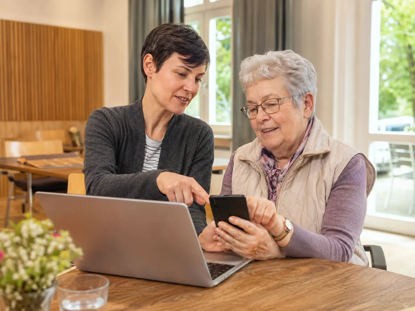 Ehrenamtliche unterstützt eine Seniorin bei Smartphone und Laptop